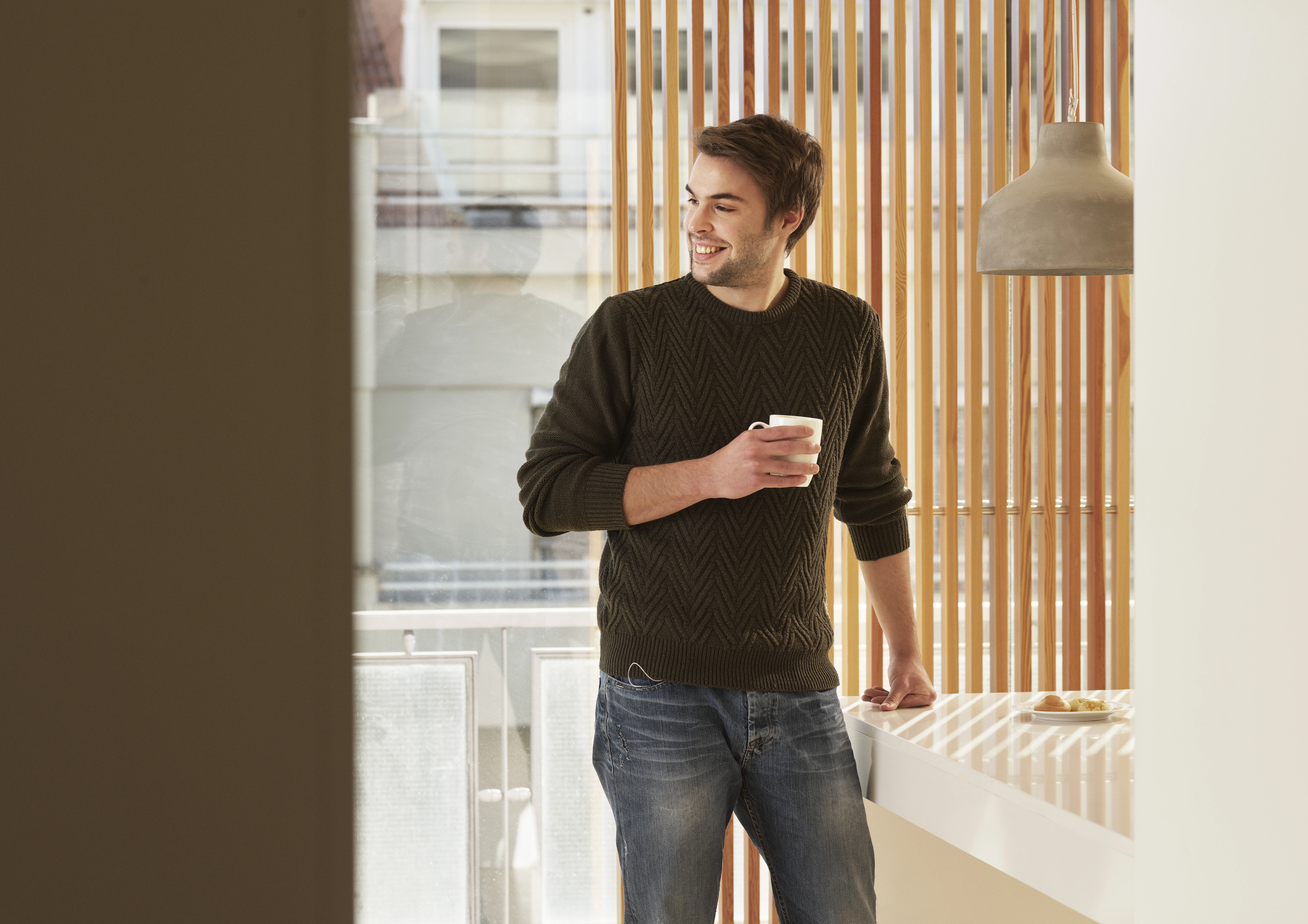 une personne debout devant une fenêtre et tenant une tasse